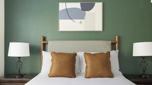 Une chambre d’hôtel avec un lit, deux lampes de chevet et un tableau abstrait accroché au mur.