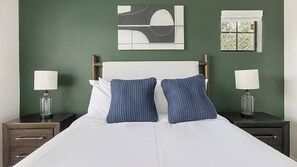 A bed with white bedding, two blue patterned pillows, and two bedside lamps on dark nightstands. - Landing | Incredible 2BD, Gym (Garland)