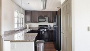 A modern kitchen with granite countertops, a stainless steel sink, a microwave, a stove, and a refrigerator. - Landing | Modern 2BD, Gym (Garland)