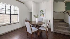A dining area with a round table, four chairs, a vase with plants, and a staircase in the background.