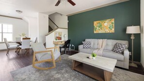 A living room with a sofa, a coffee table, a rocking chair, and a desk with a chair. - Landing | Modern 2BD, Gym (Garland)