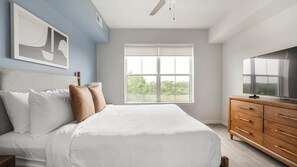 Quarto com cama, cômoda, televisão e janela com vista.