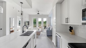 Una cocina moderna con armarios blancos, una estufa empotrada y un amplio ventanal con vistas a un balcón.