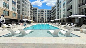 Ein Pool mit Liegestühlen und Sonnenschirmen, umgeben von mehrstöckigen Gebäuden.