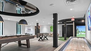 Un espace piscine intérieur moderne, équipé d’une table de billard, d’un baby-foot et d’un grand écran.