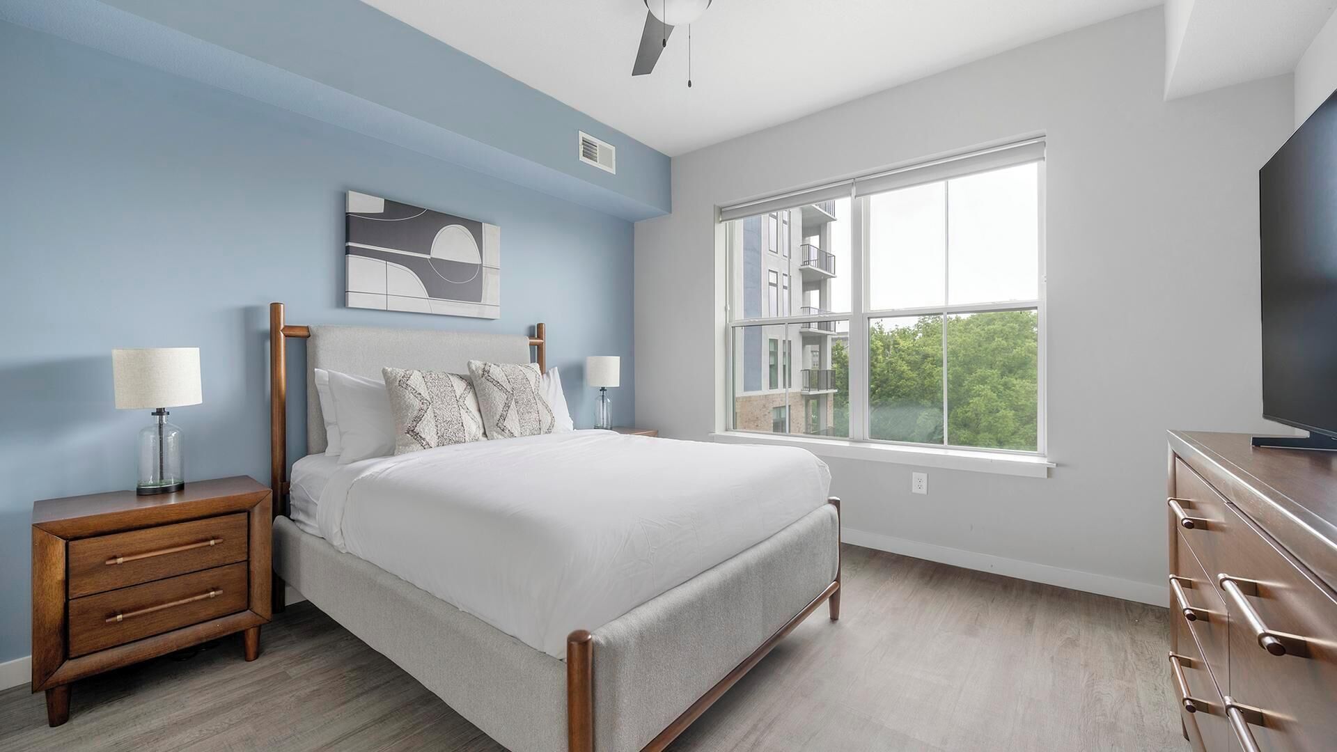 A bedroom with a bed, bedside tables, a television, and a window with a view.
