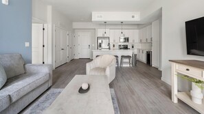 A modern living room with a grey sofa, a coffee table, and a TV on a stand. - Landing | Stylish 2BD in Cool Springs (Franklin)