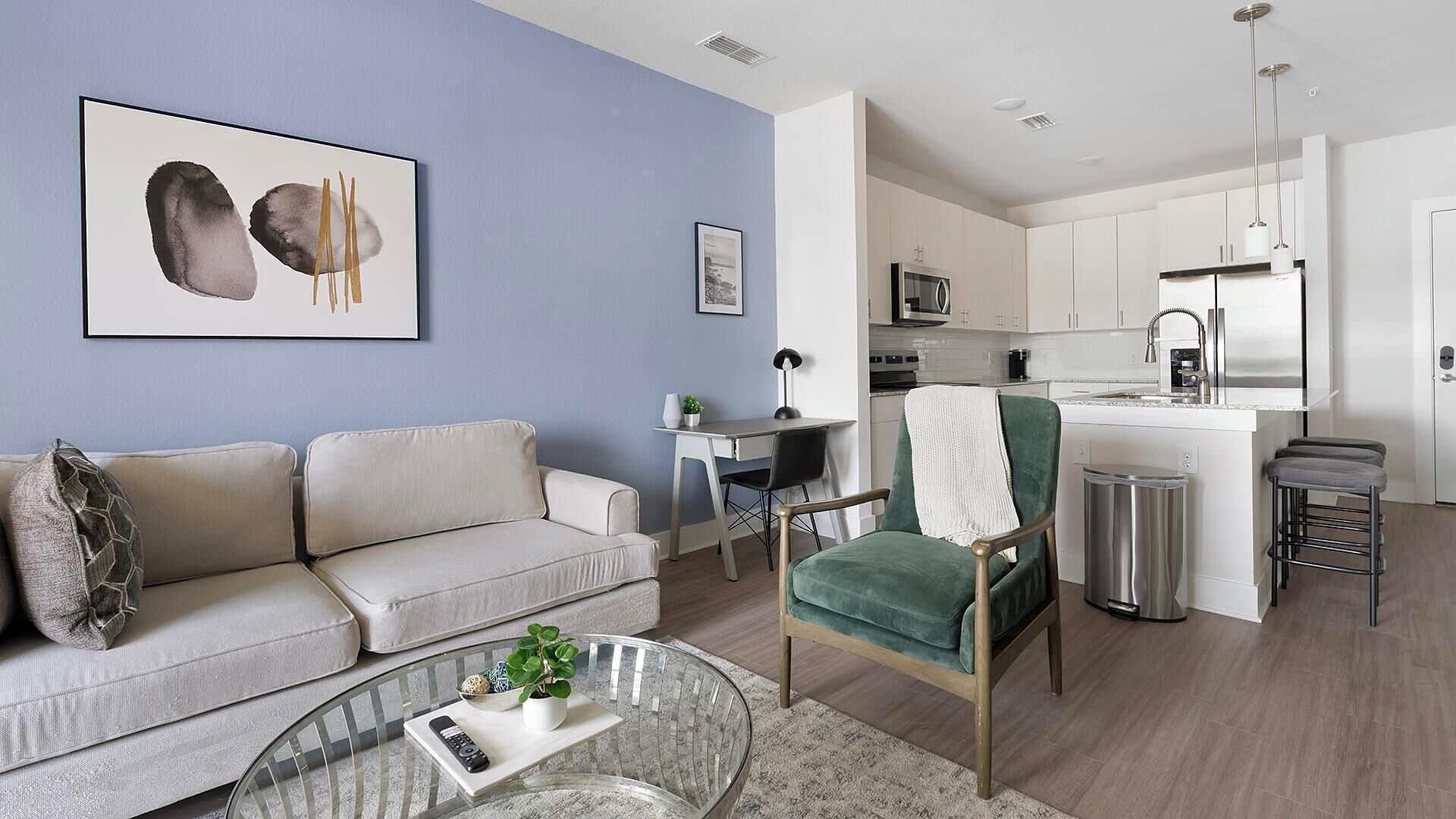 A modern living room with a sofa, a glass coffee table, and a green armchair.