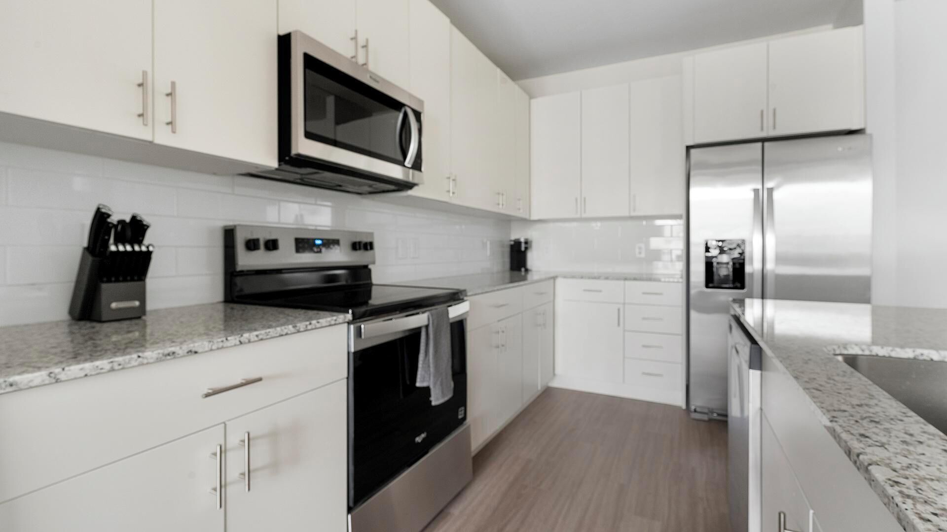 Une cuisine moderne avec des meubles blancs, un réfrigérateur en acier inoxydable, un four à micro-ondes, une cuisinière et une machine à café.