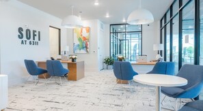 A modern office space with a reception desk, blue chairs, a round table, and large windows. - Landing | Chic 1BD, Gym, Pool (Austin)