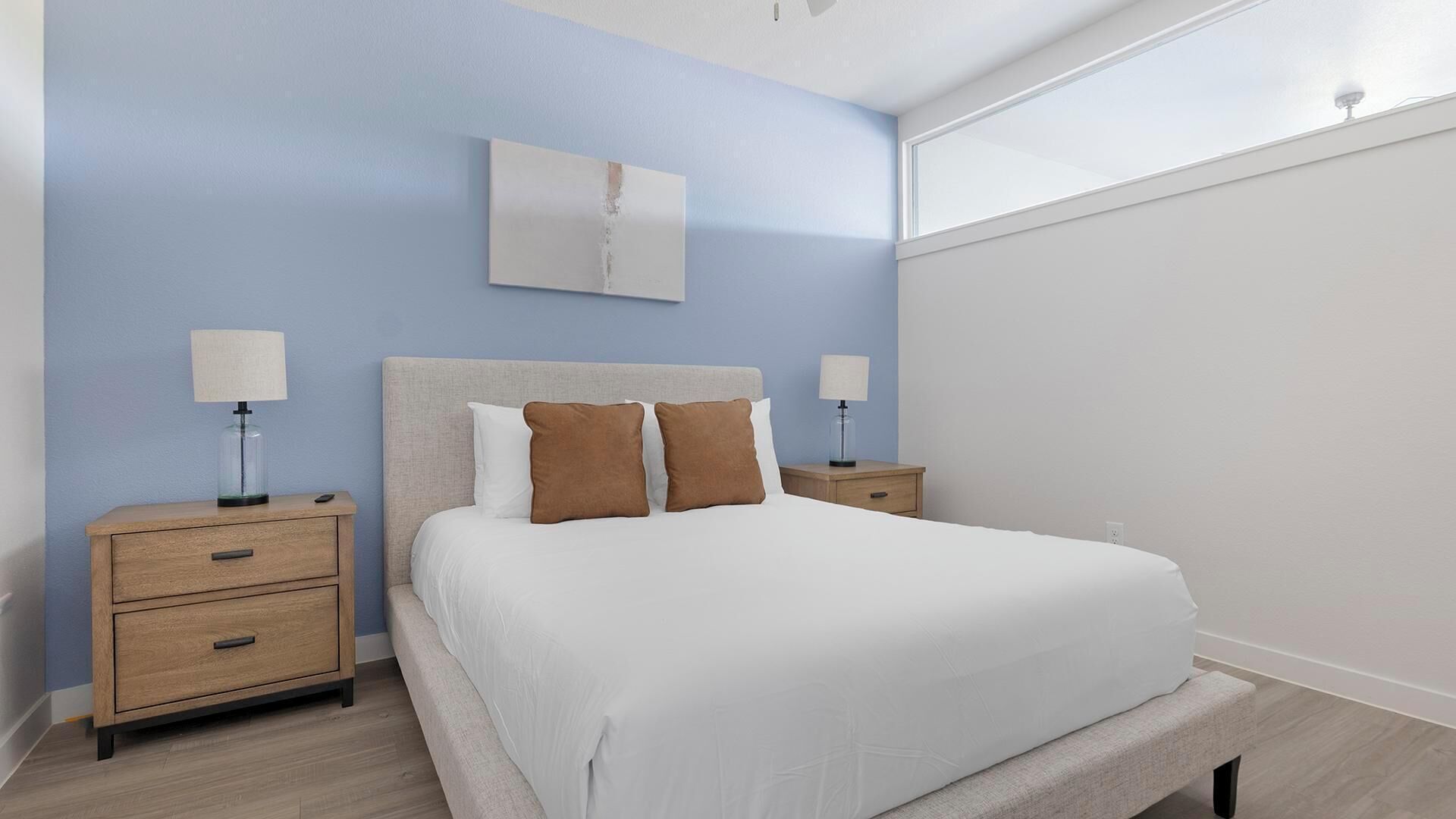 A bedroom with a bed, two bedside tables, a nightstand, a wall-mounted lamp, and a window.