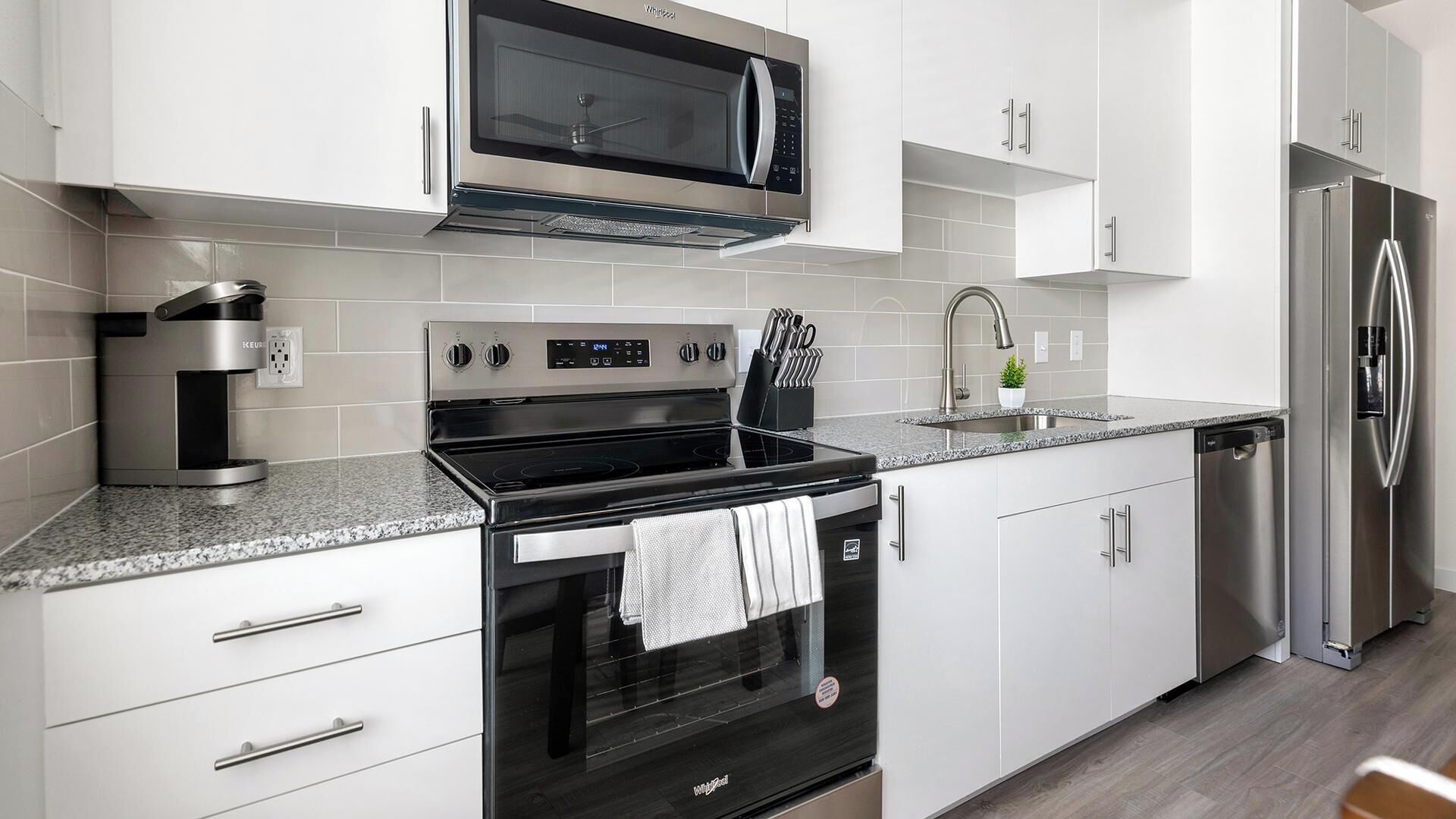 A modern kitchen with stainless steel appliances, white cabinetry, and a granite countertop.