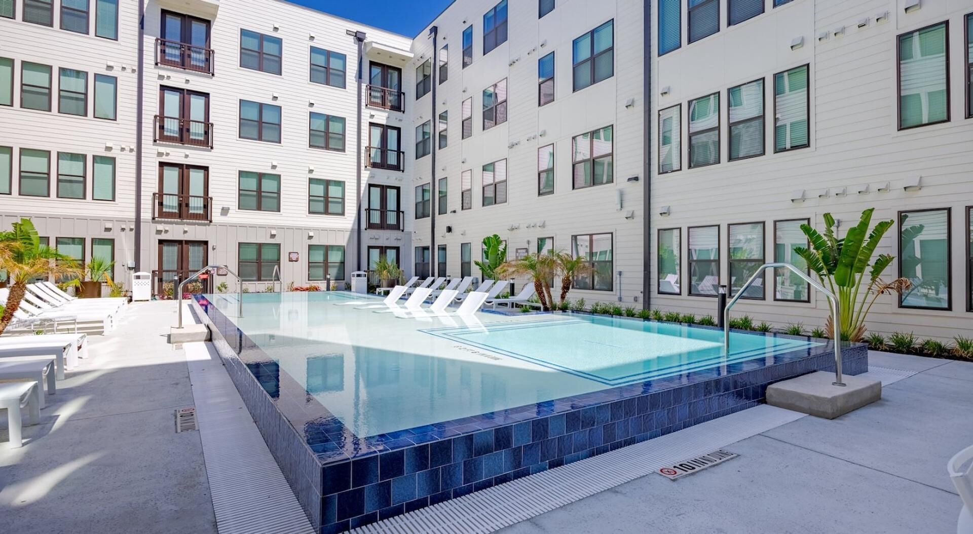 Un hotel moderno con piscina, varios balcones y una terraza de piscina limpia con baldosas.