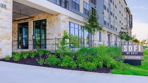 A modern building with a stone facade, large windows, and a sign indicating 'SOFI AT 6311 LEASING'. - Landing | Stunning 1BD, Gym, Pool (Austin)