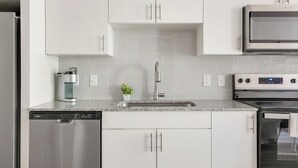 A kitchen with white cabinets, a stainless steel dishwasher, a coffee maker, a sink, and a microwave. - Landing | Stunning 1BD, Gym, Pool (Austin)