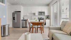 Eine moderne Küche mit weißen Schränken, Edelstahlgeräten und einem Essbereich mit Holztisch und Stühlen.