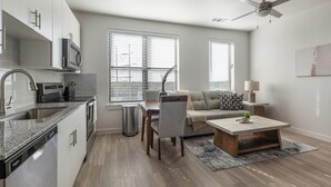 Une cuisine moderne dotée d’un four encastré, un coin repas avec une table et des chaises, un canapé gris et un ventilateur de plafond.
