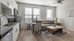 A modern kitchen with a built-in oven, a dining area with a table and chairs, a gray sofa, and a ceiling fan. - Landing | Stunning 1BD, Pool, Gym (Austin)