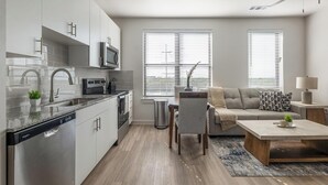 Une cuisine moderne équipée d’un lave-vaisselle, d’un four à micro-ondes et d’une cuisinière. On y trouve également un coin repas avec une table et des chaises, ainsi qu’un salon avec un canapé et une lampe.