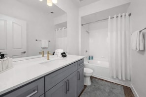 Een moderne badkamer met een wastafel met twee kommen, een toilet, een badkuip en een douchegordijn.