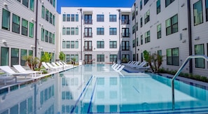 A modern hotel with a central swimming pool surrounded by lounge chairs and palm trees. - Landing | Stunning 1BD, Pool, Gym (Austin)