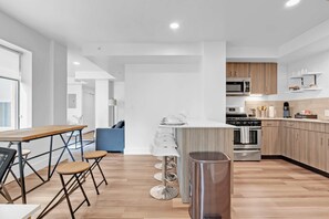 A modern kitchen with a central island, stainless steel appliances, and a dining area with a wooden table and bar stools. - Tulsa 2BR City Stay  Rooftop Lounge, Gym & Pet Friendly (Tulsa)
