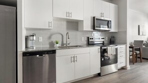 A modern kitchen with a dishwasher, stove, microwave, and a coffee maker. - Landing | Modern 1BD, Gym, Pool (Austin)