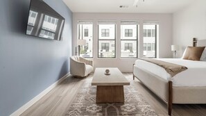 Ein modernes Schlafzimmer mit einem Bett, einem Schlafsofa, einem Couchtisch und einem an der Wand befestigten Fernseher.