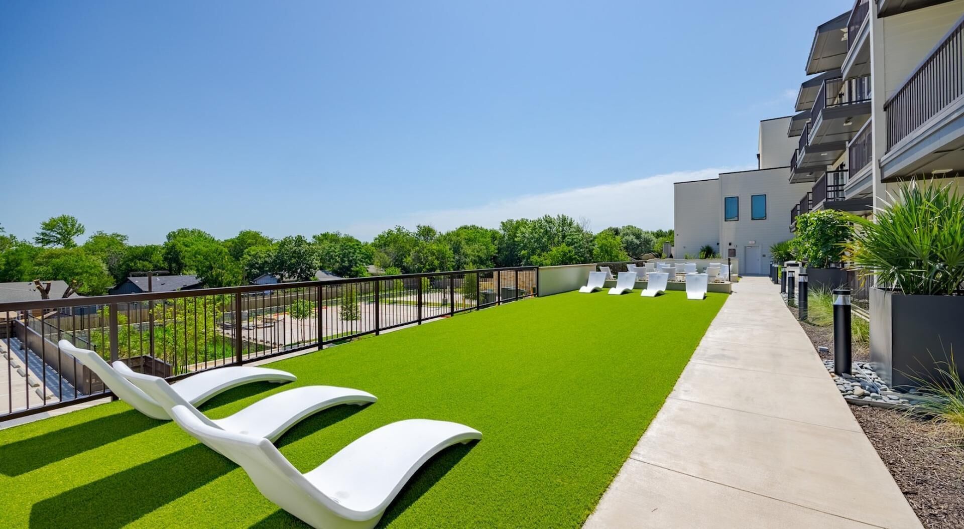 A rooftop terrace with artificial grass, white lounge chairs, and a concrete pathway.