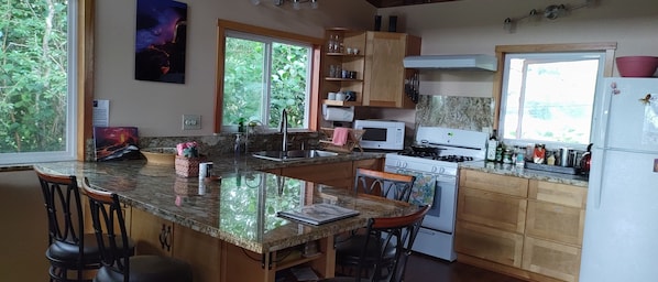 A kitchen with granite countertops, wooden cabinets, a stove, a microwave, and a sink. - Aloha Sanctuary: Charming 1-bedroom studio in Kea'au near beautiful Kaloli Point (Kea'au)