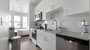 A modern kitchen with white cabinetry, a stainless steel sink, a microwave, an oven, and a dishwasher. - Landing | Chic Studio, Gym, Pool (Austin)