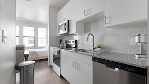 Eine moderne Küche mit weißen Schränken, einer Edelstahlspüle, einer Mikrowelle, einem Backofen und einem Geschirrspüler.