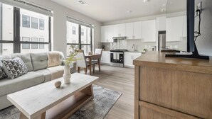 A modern kitchen with white cabinets, a wooden island, and a dining area with a sofa and coffee table. - Landing | Amazing 1BD, Pool, Gym (Austin)