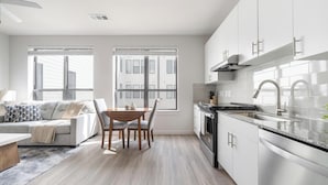 A modern kitchen with white cabinets, a stainless steel sink, and a dining area with a wooden table and chairs. - Landing | Amazing 1BD, Pool, Gym (Austin)