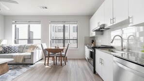 Eine moderne Küche mit weißen Schränken, einer Edelstahlspüle und einem Essbereich mit einem Holztisch und Stühlen.