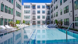 A modern hotel with a central swimming pool surrounded by lounge chairs and palm trees. - Landing | Amazing 1BD, Pool, Gym (Austin)