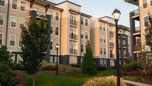 Un immeuble résidentiel à plusieurs étages doté d’une cour intérieure, entouré d’arbres et d’une pelouse bien entretenue.