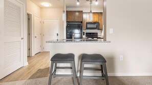 A kitchen with a central island, two bar stools, wooden cabinets, a refrigerator, a microwave, and a stove.