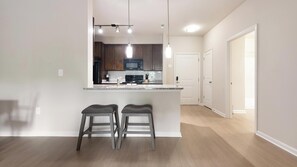 A modern kitchen with dark wood cabinets, a central island with stools, and pendant lighting. - Landing | Amazing 1BD, Pool, Gym (Manassas Park)