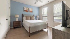 A bedroom with a bed, nightstands, a ceiling fan, a window with blinds, and a television.