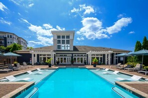 A hotel with a central swimming pool, lounge chairs, and a covered patio area.