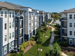 A multi-story residential building with balconies, a central courtyard, and a parking area. - Landing | Chic 1BD, Gym, Pool (Manassas Park)