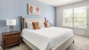 Une chambre à coucher comprenant un lit, deux tables de chevet, une fenêtre et une œuvre d’art murale.