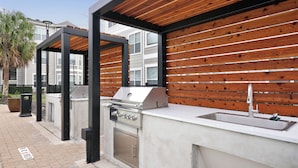 Un espace cuisine extérieur comprenant un barbecue, un évier et un fond en panneaux de bois.