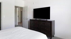 Un dormitorio con una cama, un aparador oscuro con televisor de pantalla plana y una puerta que da a otra habitación.