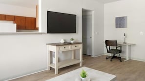 Ein modernes Wohnzimmer mit Schreibtisch aus Holz, einem Sessel, einem Flachbildfernseher und einer kleinen Pflanze.