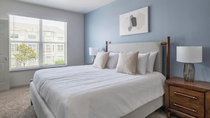 A bedroom with a large bed, two bedside tables with lamps, a window with blinds, and a wall-mounted artwork. - Landing | Stunning 2BD, Gym, Yoga Studio (Humble)