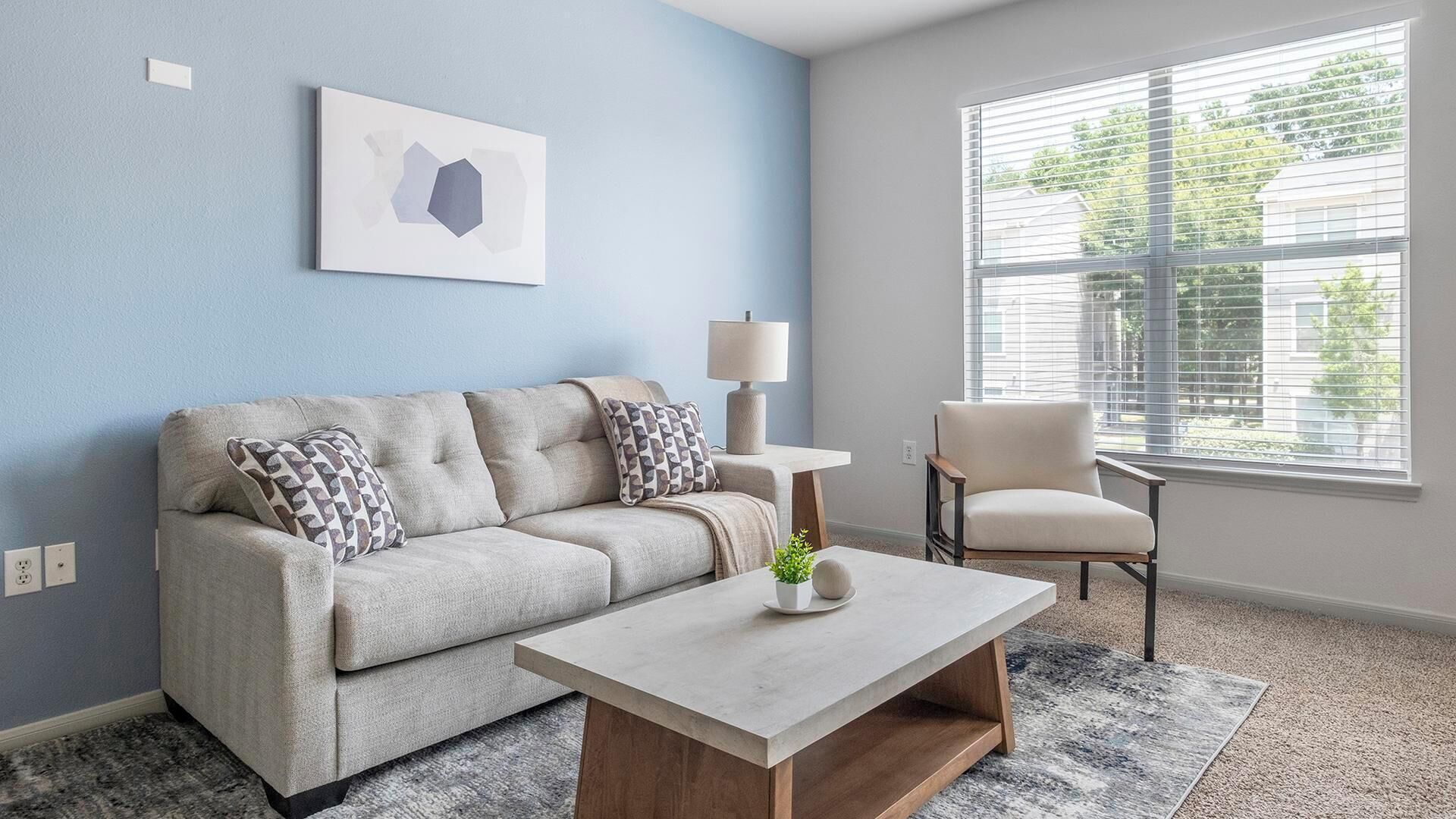 A living room with a sofa, a coffee table, a chair, a lamp, and a window with blinds.