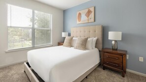 A bedroom with a large bed, a nightstand, a lamp, a window with blinds, and a wall art piece. - Landing | Incredible 2BD, Pool, Yoga Studio (Humble)