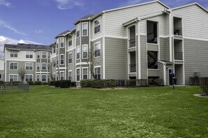 A multi-story residential building with a flat roof, large windows, and a well-maintained lawn. - Landing | Incredible 2BD, Pool, Yoga Studio (Humble)